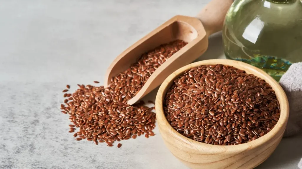 लकड़ी के बर्तन और स्कूप में भरे अलसी (Flaxseed) के बीज, पास में कांच की बोतल रखी हुई