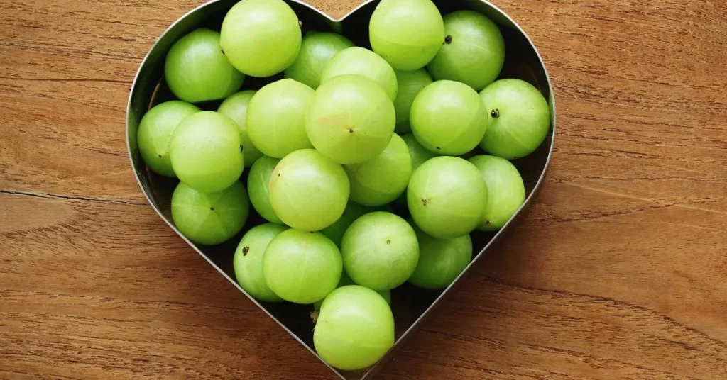 लकड़ी की मेज़ पर दिल के आकार के बर्तन में रखे ताज़े हरे आंवला