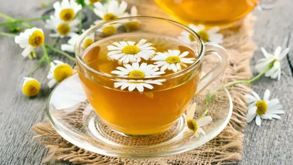 Chamomile Tea का प्याला जिसमें ताजे सफेद फूल तैर रहे हैं, लकड़ी की मेज पर रखा हुआ