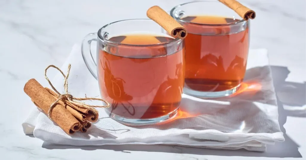 गर्म cinnamon water से भरे दो ग्लास और पास रखी दालचीनी स्टिक।