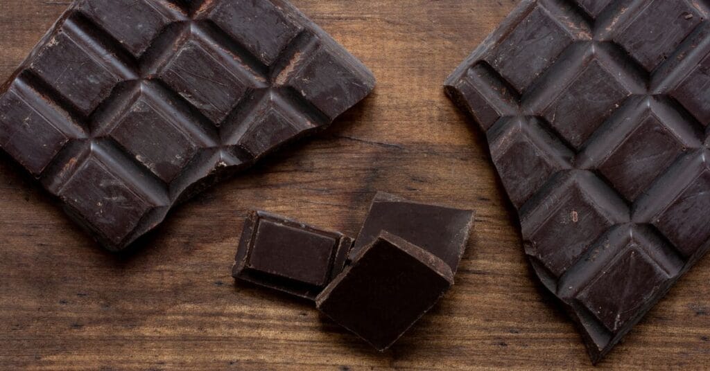 लकड़ी की सतह पर रखी डार्क चॉकलेट के टुकड़े, जिनमें हाई कोको कंटेंट दिखाई दे रहा है
