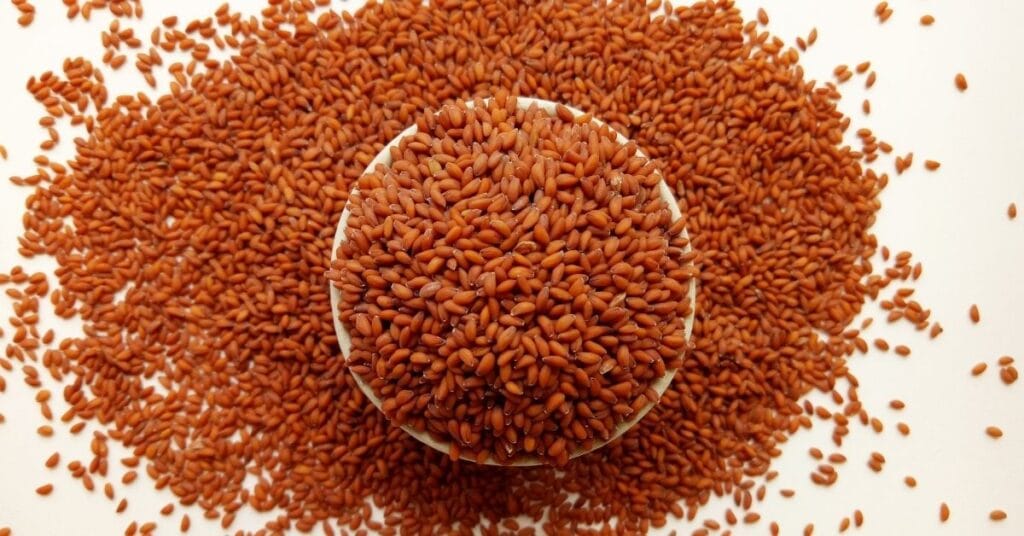 कटोरी में रखे हुए लाल रंग के Halim Seeds (Garden Cress Seeds) का क्लोज़-अप दृश्य।