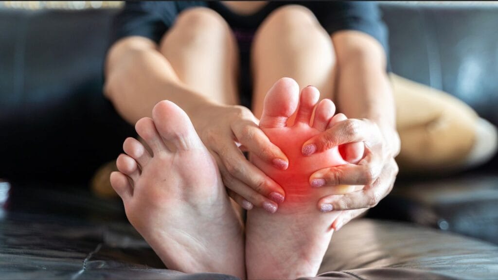 एक व्यक्ति पैर के अगले हिस्से (बॉल ऑफ फुट) में दर्द महसूस करते हुए उसे हाथों से पकड़ रहा है, जहां लाल रंग से दर्द और सूजन दिखाई गई है।